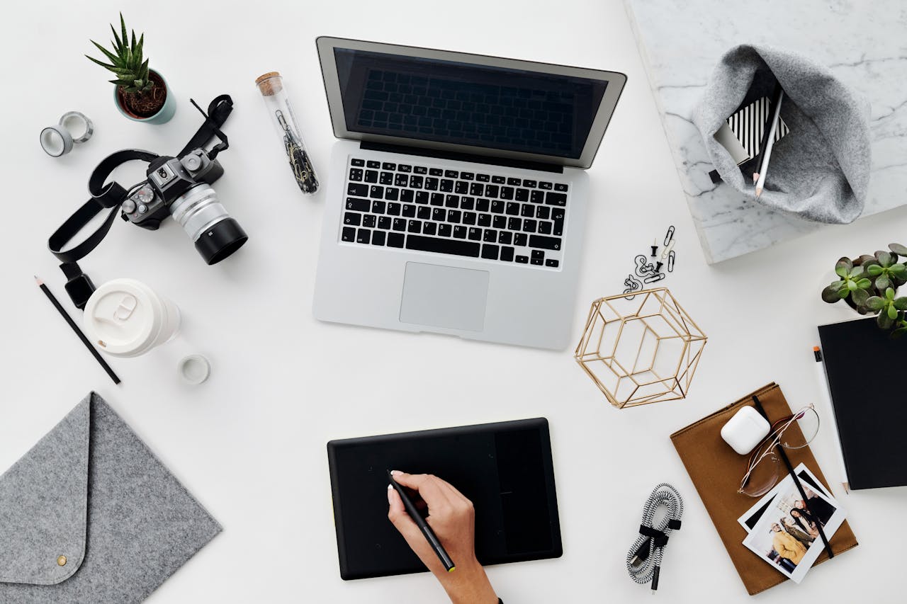 A stylish overhead view of a creative workspace featuring digital devices, drawing tablet, and stationery.